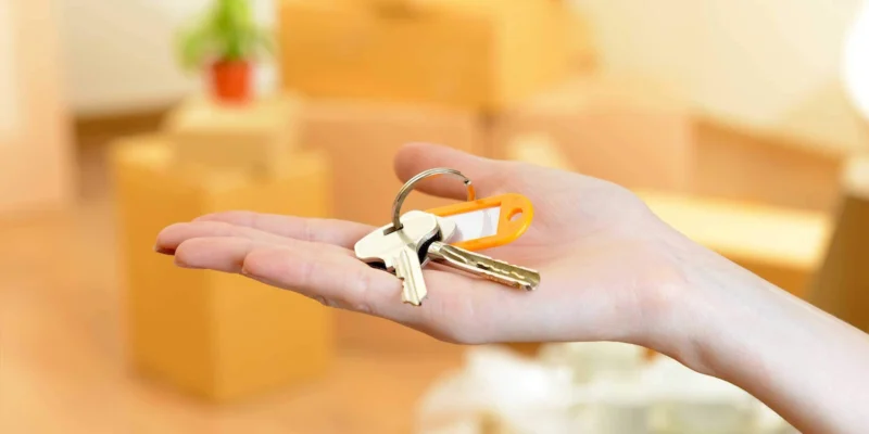Hand holding house keys with moving boxes in the background